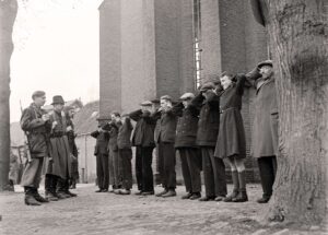 oude zwart wit foto waarbij drie mannen een rij collaborateurs voor een kerk bewaken. 